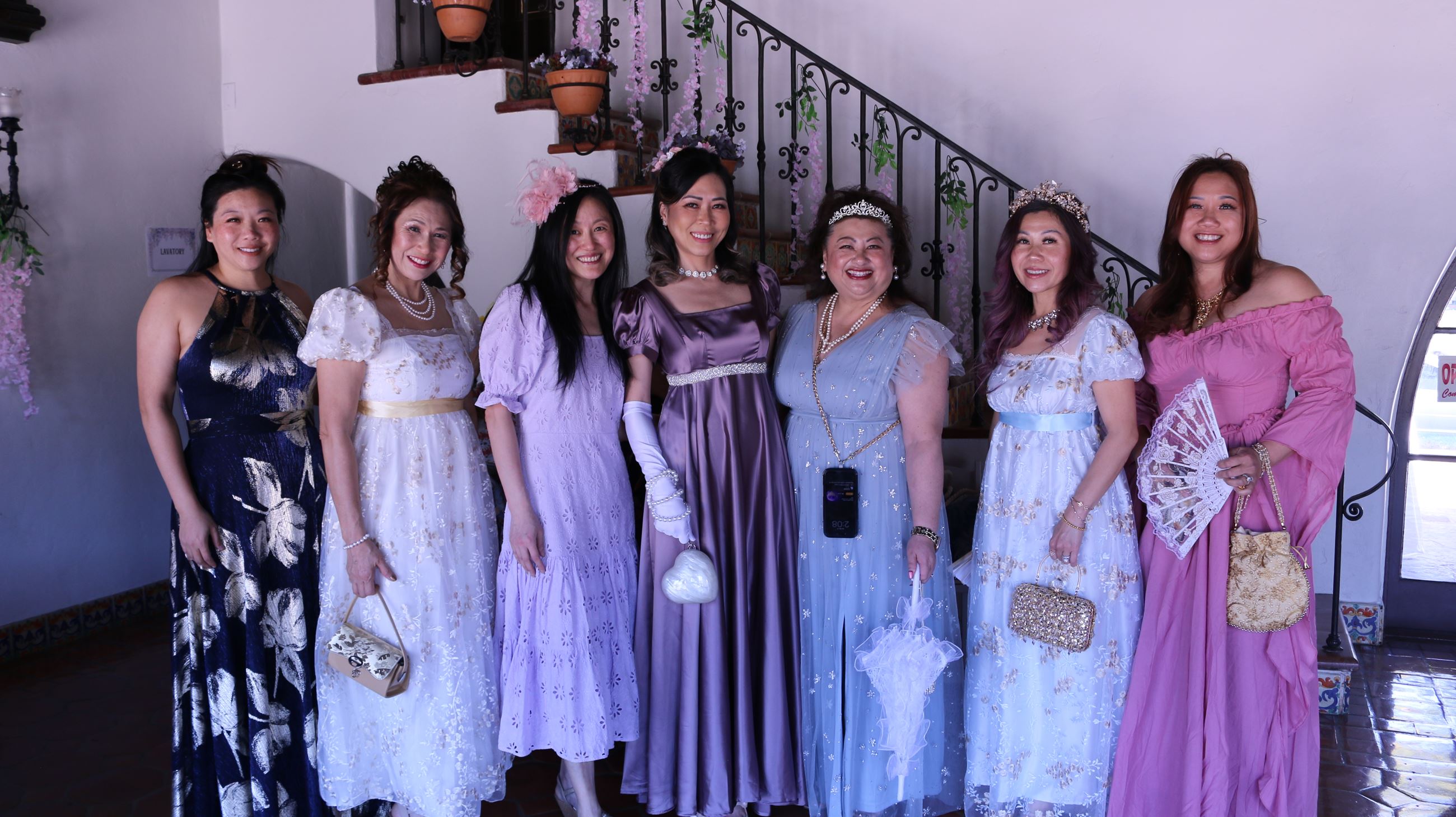 Group of seven adults in long gowns smile at camera facing front